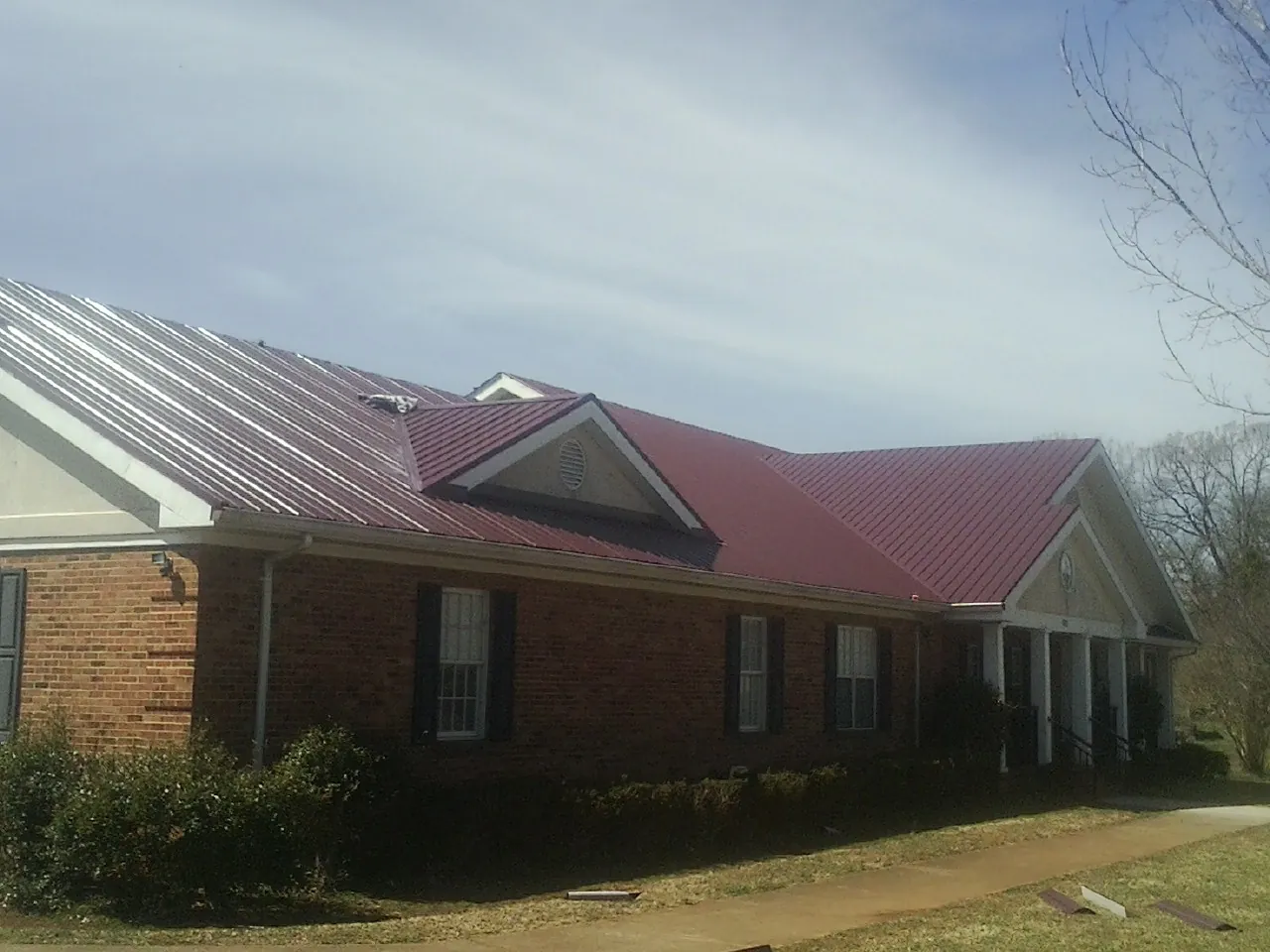 Red metal roof with gabled entries on a long brick building, from a Hail Damage Roof Repair job in Soquel