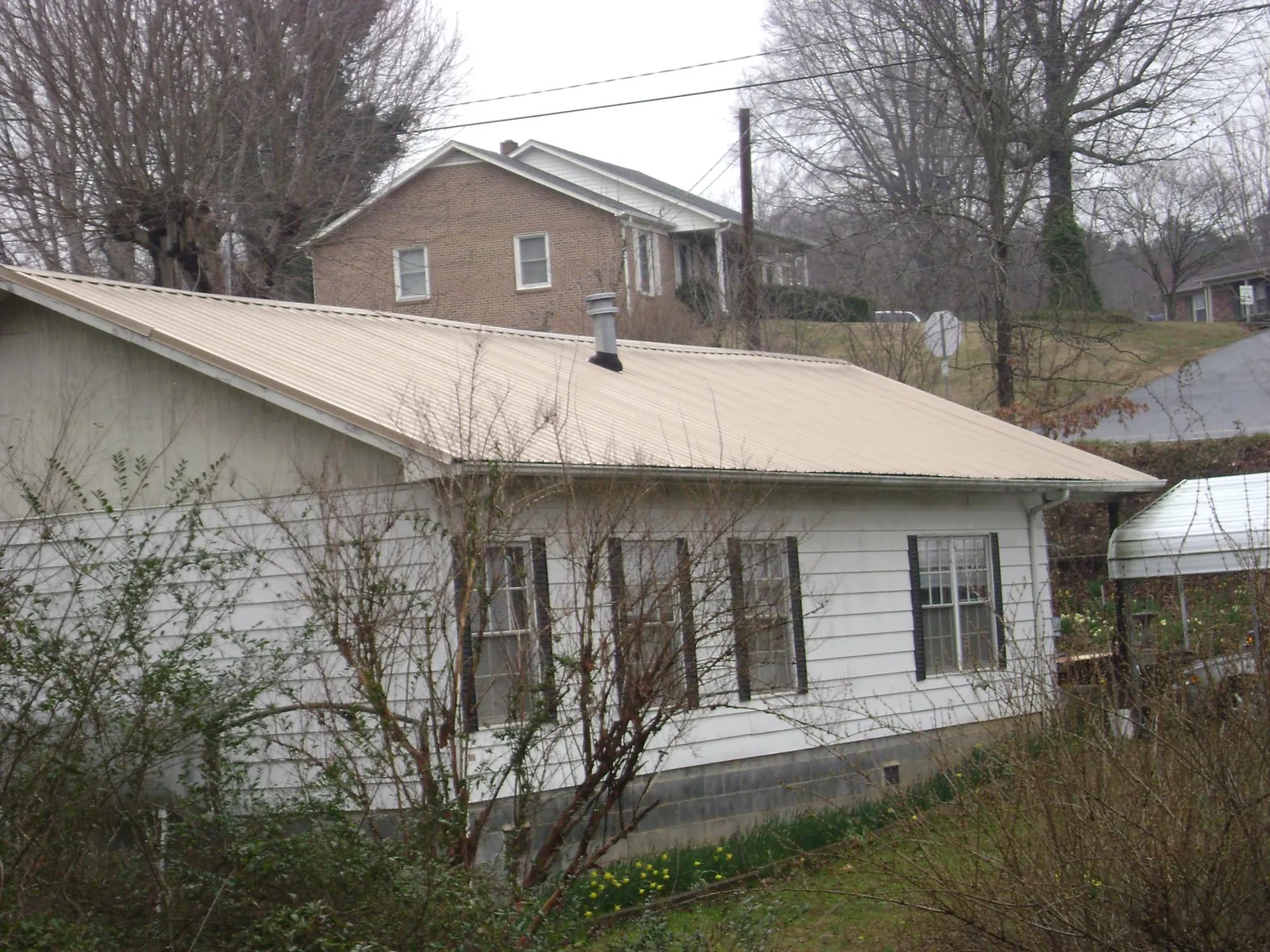 Tan metal roof on a white sided house set into a hillside — Commercial Roofing by Roofing Brothers in Soquel